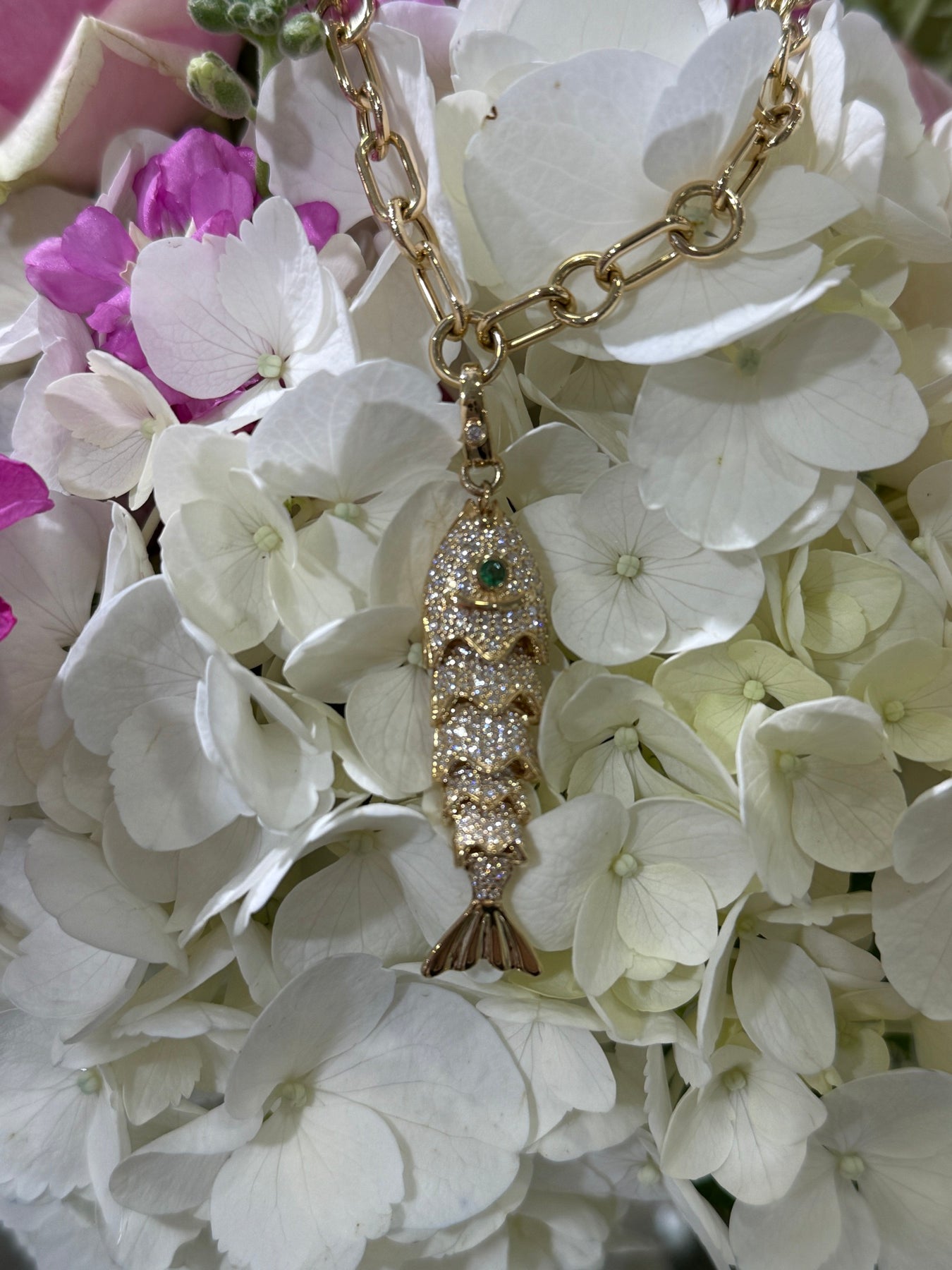 Gold fish pendant necklace arranged on white hydrangeas